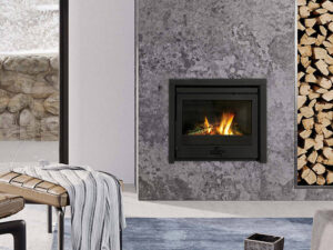 Insert à bois en fonte Dovre 2520 S/B dans une cheminée en pierre grise, bûcher à côté