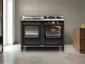 Cuisinière mixte Archambaud Légende 120 noire et laiton dans une cuisine de loft contemporain, sol en pierre claire