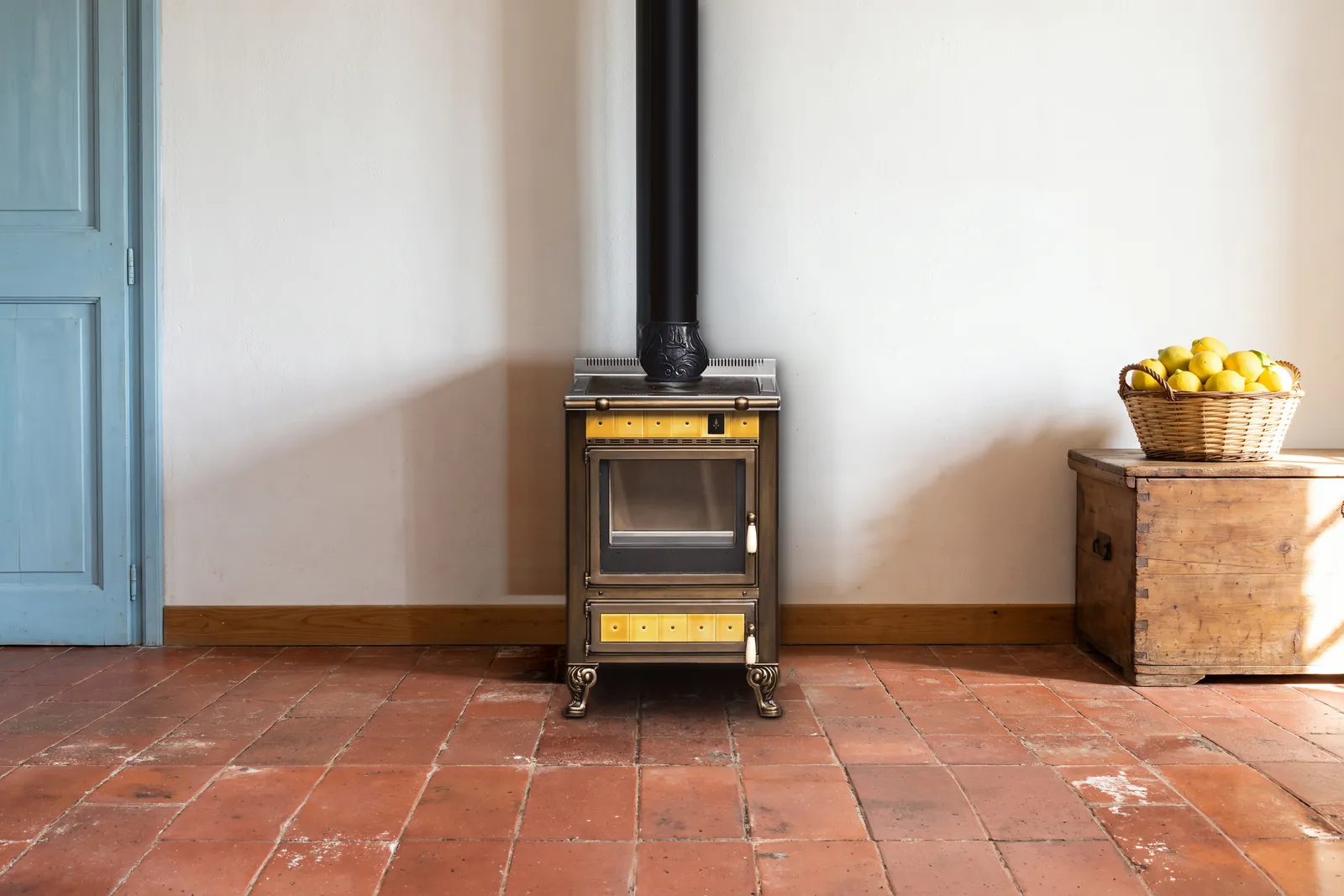 Cuisinière à bois Archambaud Origine 60 en faïence jaune ocre dans une cuisine de campagne italienne, sol en tomettes de terre cuite