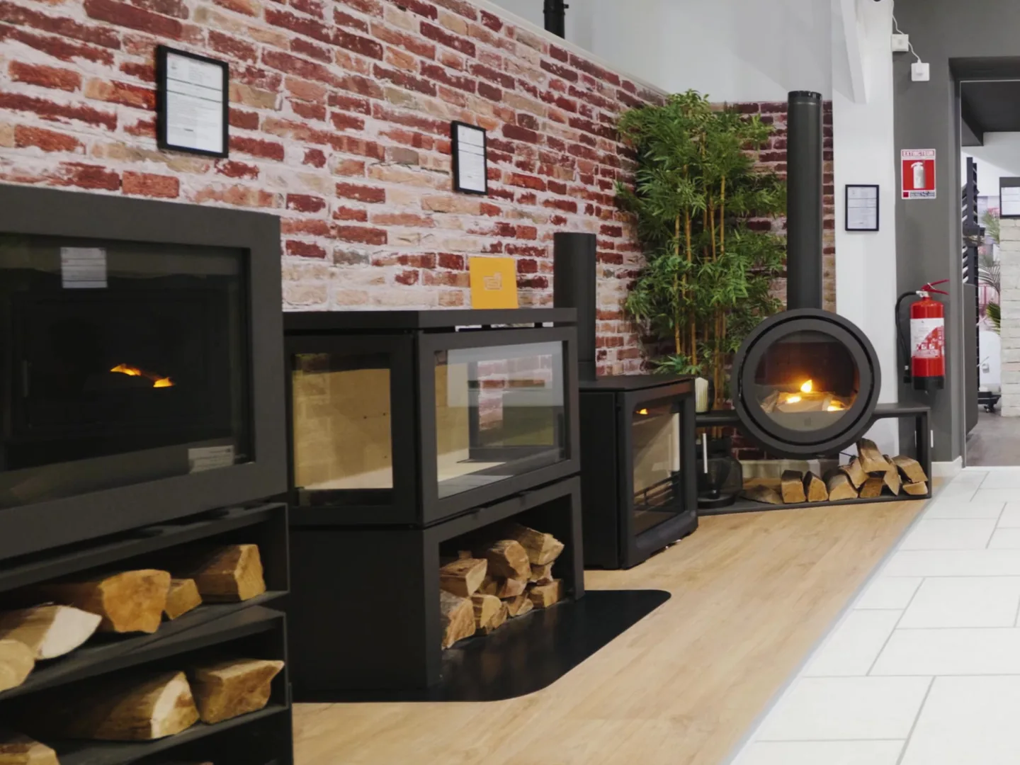 Poêles à bois posés sur des bancs à bûches devant le mur de briques du showroom de Vitré